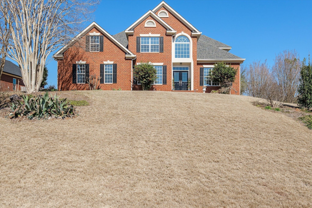 view of front of home with brick siding, a front lawn, and roof with shingles