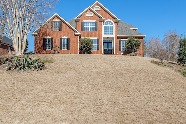 view of front of home with brick siding, a front lawn, and roof with shingles