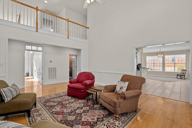 living room with baseboards, visible vents, a towering ceiling, wood finished floors, and ceiling fan with notable chandelier