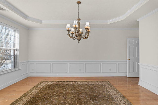 interior space with crown molding, a raised ceiling, a decorative wall, a chandelier, and light wood-type flooring