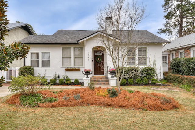 view of front of house with stucco siding, a chimney, roof with shingles, and a front yard