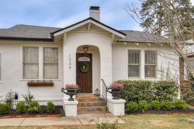 property entrance featuring a chimney, stucco siding, and a shingled roof