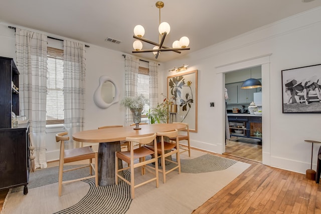 dining room featuring visible vents, light wood-style flooring, ornamental molding, an inviting chandelier, and baseboards