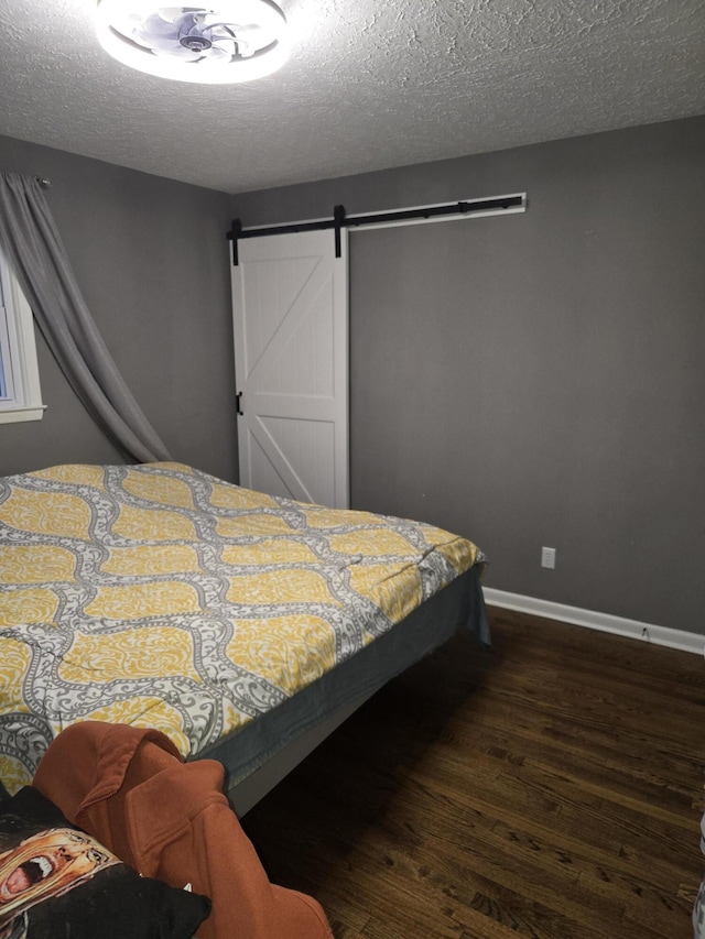 bedroom with a textured ceiling, a barn door, dark wood-style flooring, and baseboards