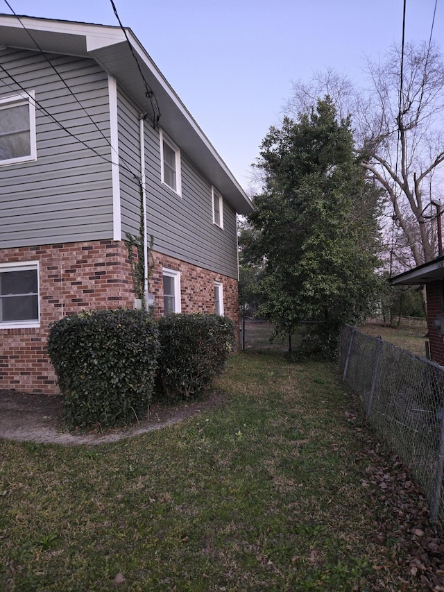 view of property exterior with a yard, brick siding, and fence