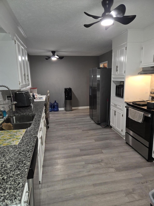 kitchen with light wood finished floors, stainless steel appliances, white cabinetry, a sink, and under cabinet range hood