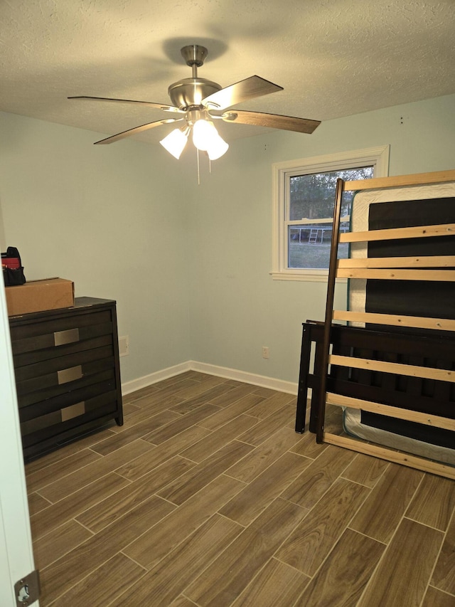 bedroom with ceiling fan, baseboards, a textured ceiling, and wood finish floors