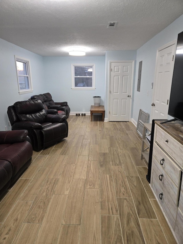 living room with light wood finished floors, baseboards, visible vents, and a textured ceiling