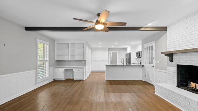 unfurnished living room with ceiling fan, built in desk, a fireplace, beam ceiling, and wood-type flooring