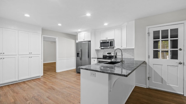 kitchen with white cabinets, sink, light wood-type flooring, kitchen peninsula, and stainless steel appliances