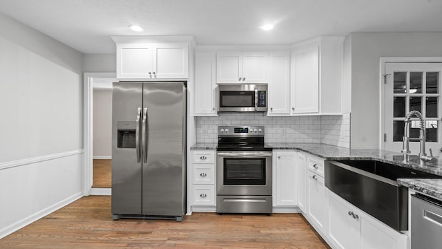 kitchen with white cabinetry, sink, dark stone countertops, appliances with stainless steel finishes, and hardwood / wood-style flooring