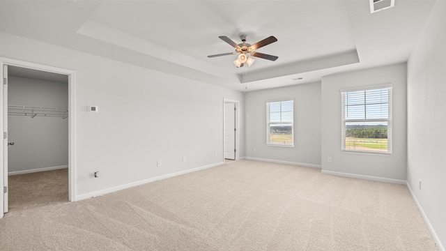 unfurnished bedroom featuring ceiling fan, a walk in closet, a tray ceiling, and light carpet