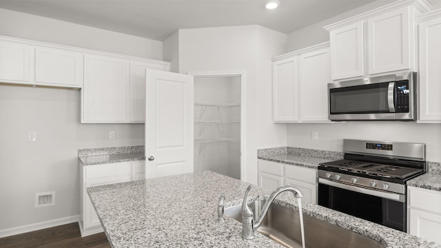 kitchen with light stone counters, stainless steel appliances, sink, and white cabinets