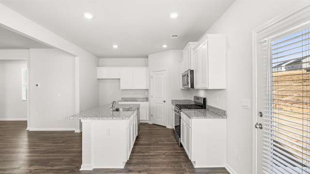 kitchen featuring sink, stainless steel appliances, light stone counters, white cabinets, and a center island with sink