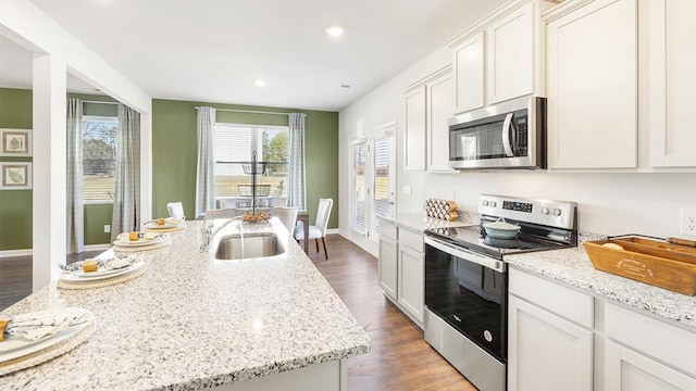 kitchen with sink, white cabinets, stainless steel appliances, light stone countertops, and a center island with sink