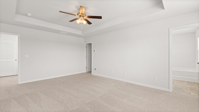 unfurnished room featuring ceiling fan, a tray ceiling, and light carpet