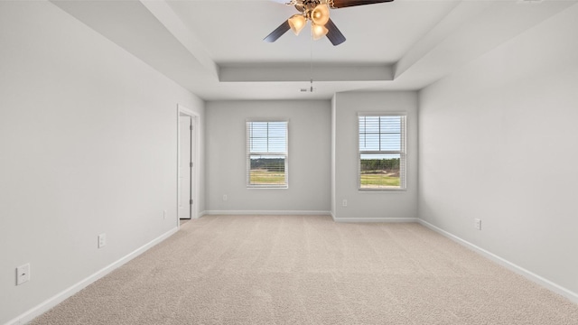 carpeted empty room with a raised ceiling and ceiling fan