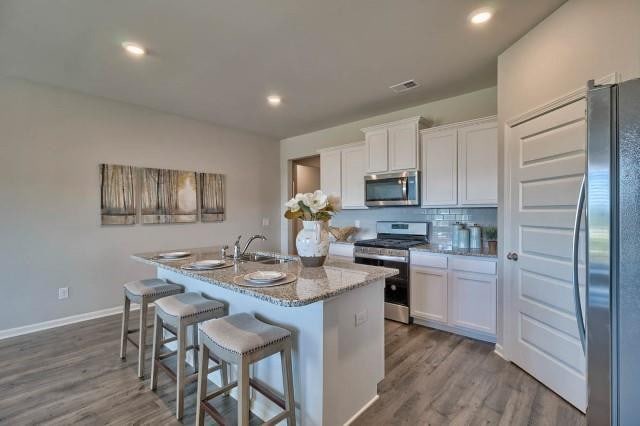 kitchen with white cabinetry, stainless steel appliances, light stone countertops, and a kitchen island with sink