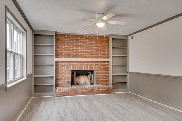 unfurnished living room with light wood-type flooring, a textured ceiling, ceiling fan, built in features, and a fireplace