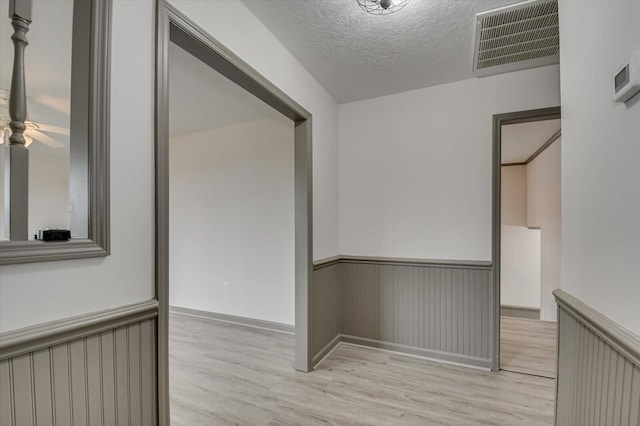 corridor featuring light wood-type flooring and a textured ceiling