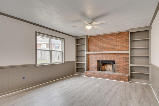 unfurnished living room with light wood-type flooring, a brick fireplace, built in shelves, a textured ceiling, and ceiling fan