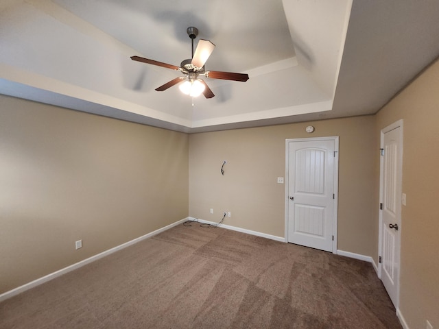 carpeted empty room with ceiling fan and a tray ceiling