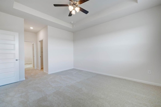 empty room with ceiling fan, a raised ceiling, and light carpet