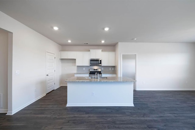 kitchen with light stone countertops, stainless steel appliances, dark wood-type flooring, a center island with sink, and white cabinetry