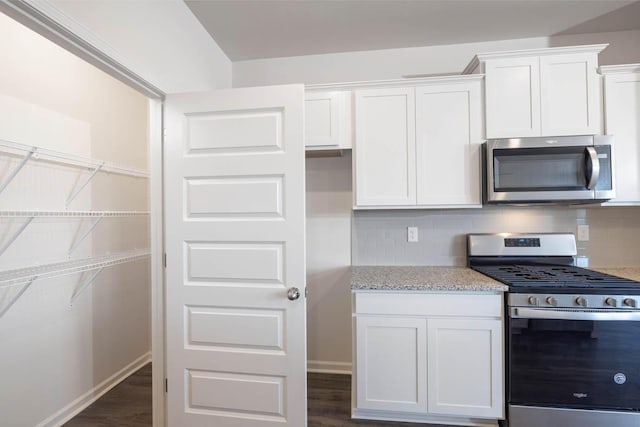 kitchen featuring white cabinets, light stone countertops, tasteful backsplash, dark hardwood / wood-style flooring, and stainless steel appliances