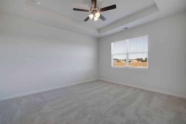 carpeted spare room with a tray ceiling and ceiling fan