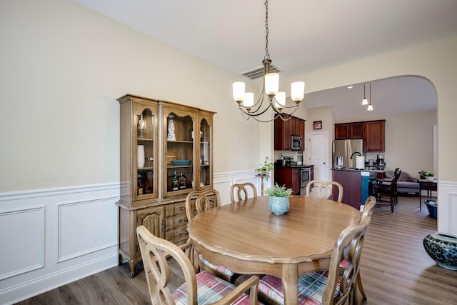 2306 Peach Blossom Pass, Hephzibah, GA 30815 - dining area with arched walkways, a wainscoted wall, dark wood-style floors, a chandelier, and a decorative wall