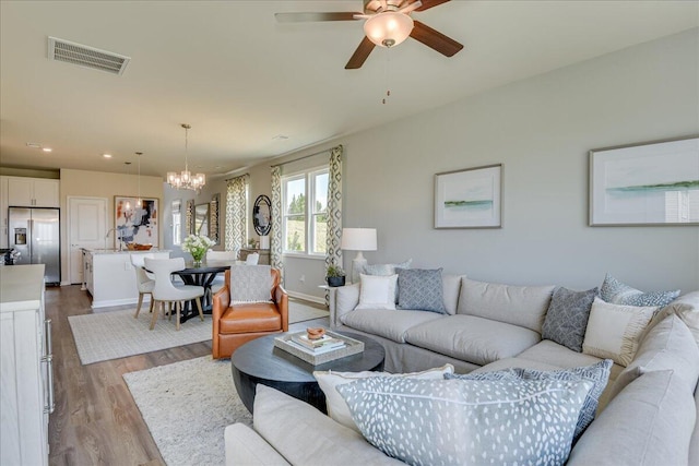 living room with ceiling fan with notable chandelier and light wood-type flooring