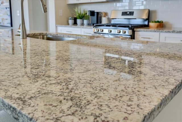 interior details with light stone countertops, sink, stainless steel gas range oven, decorative backsplash, and white cabinets