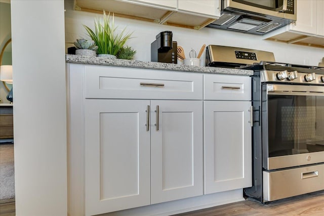 details featuring light stone counters, white cabinetry, stainless steel appliances, and light hardwood / wood-style flooring