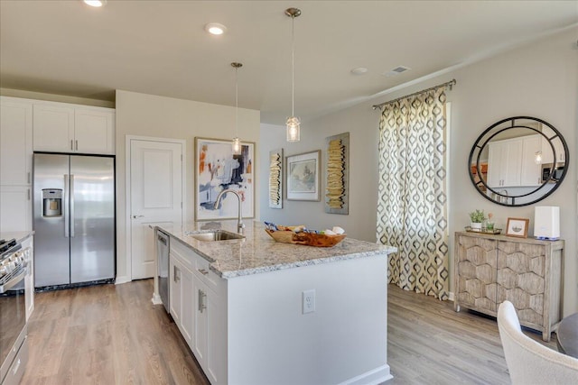 kitchen with white cabinetry, sink, stainless steel appliances, decorative light fixtures, and a center island with sink