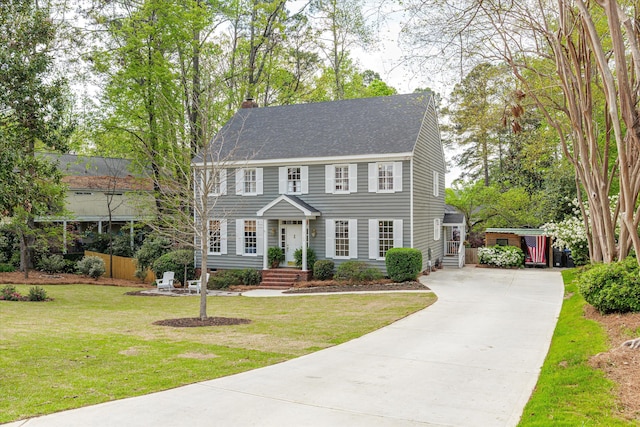 colonial inspired home featuring roof with shingles, driveway, a chimney, and a front yard