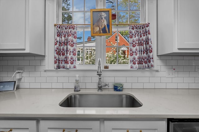 kitchen featuring stainless steel dishwasher, decorative backsplash, light stone countertops, white cabinets, and a sink