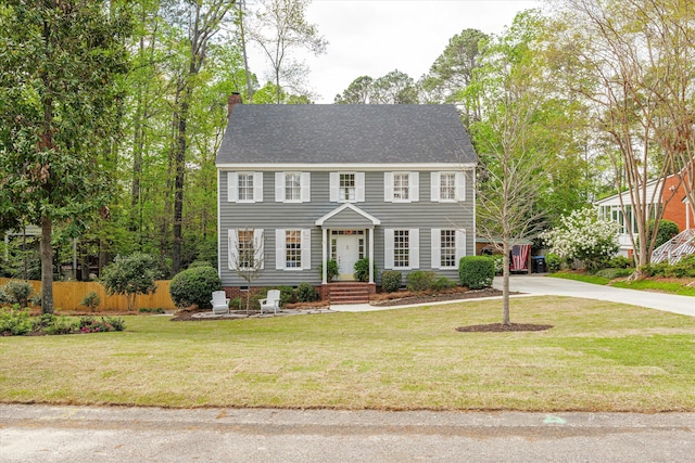 colonial-style house with a front yard, fence, driveway, and a chimney