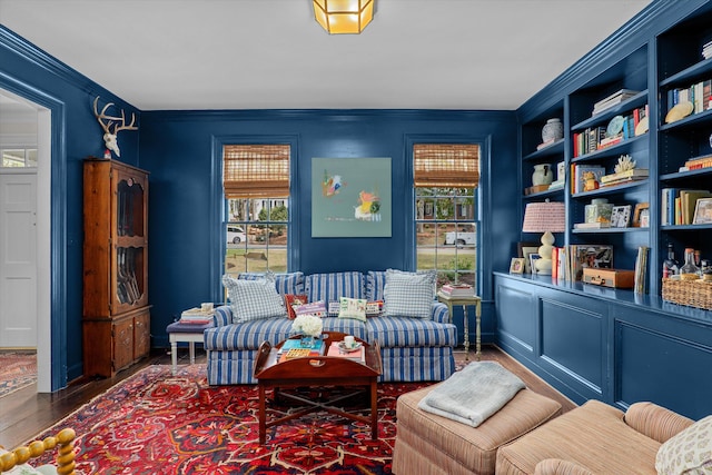sitting room featuring built in shelves, ornamental molding, and wood finished floors