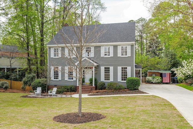 colonial-style house featuring fence, a shingled roof, driveway, and a front lawn