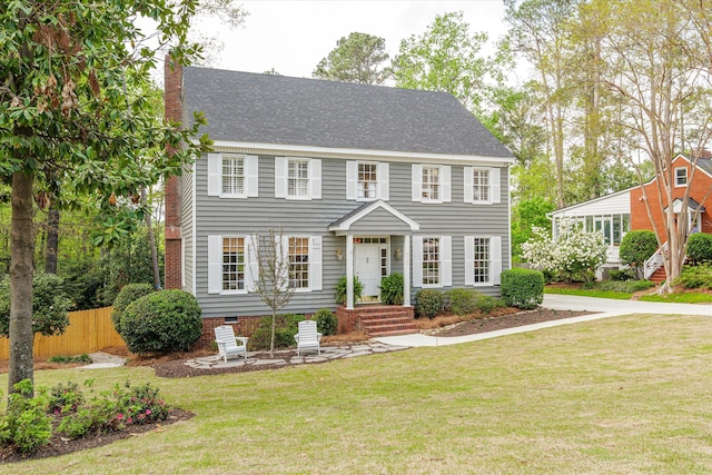 colonial house featuring roof with shingles, fence, a chimney, and a front yard