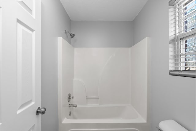 bathroom with a textured ceiling, toilet, and bathing tub / shower combination