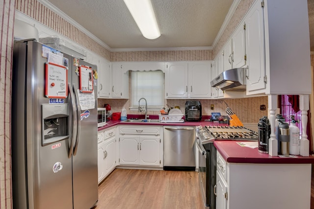 kitchen with under cabinet range hood, stainless steel appliances, a textured ceiling, white cabinetry, and a sink