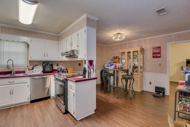 kitchen featuring visible vents, a sink, under cabinet range hood, stainless steel appliances, and wallpapered walls