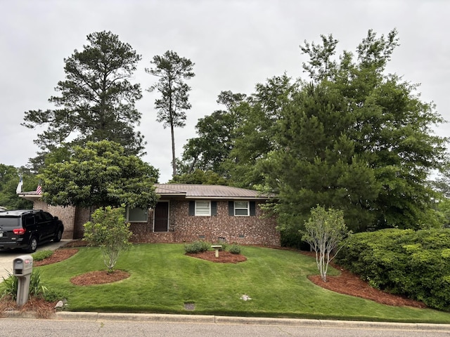 view of front of property with a front lawn, brick siding, metal roof, and driveway