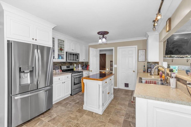 kitchen featuring appliances with stainless steel finishes, a sink, tasteful backsplash, white cabinetry, and ornamental molding