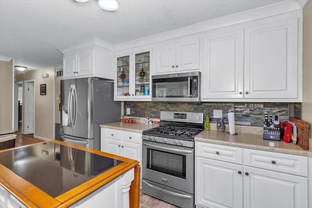 kitchen featuring stainless steel appliances, white cabinets, tasteful backsplash, glass insert cabinets, and light countertops