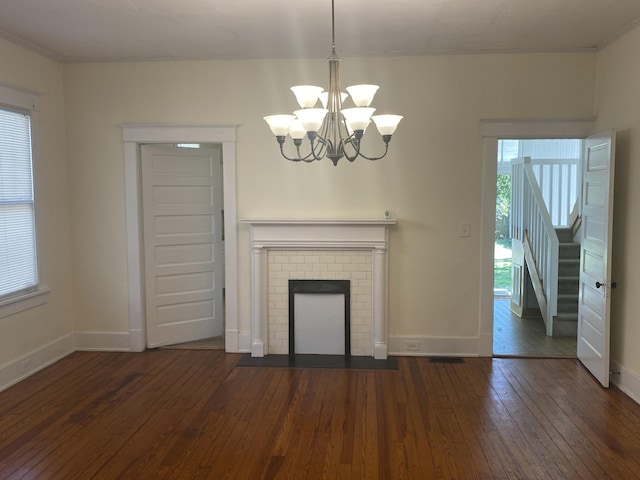 unfurnished living room with a brick fireplace, an inviting chandelier, plenty of natural light, and dark wood-type flooring