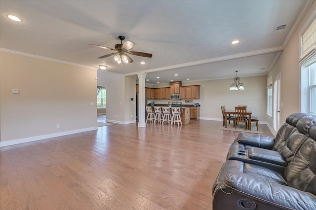 living room featuring light wood-style floors, baseboards, ornamental molding, and ceiling fan with notable chandelier
