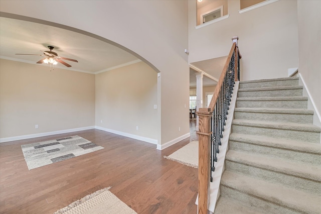 staircase with crown molding, wood finished floors, baseboards, arched walkways, and a ceiling fan